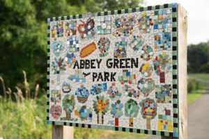The sign for Abbey Green park in Polesworth, a mosaic design with lots of trees.